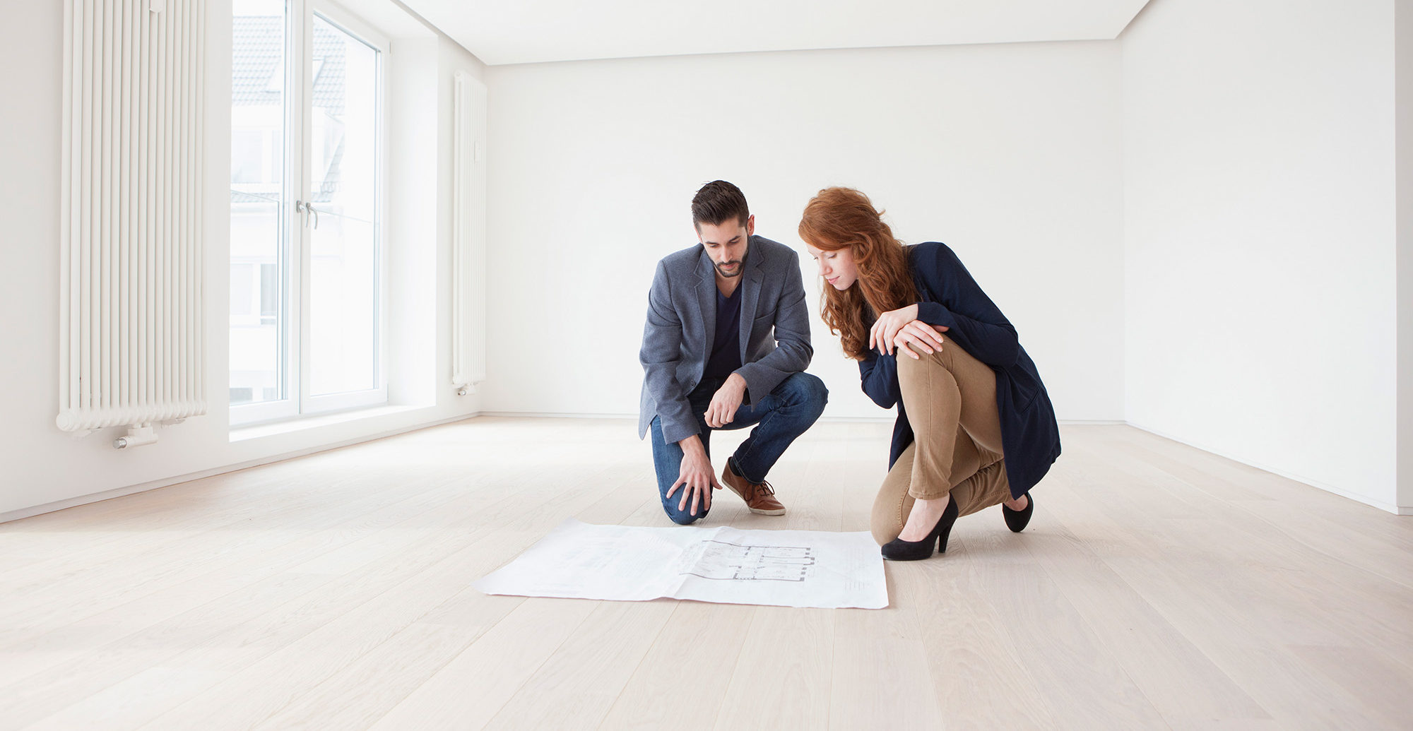 Young couple sitting on floor of their new flat, looking at ground plan